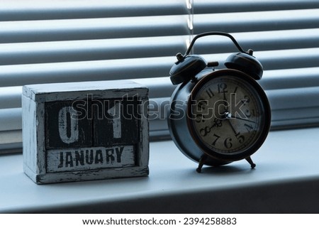 Morning of January 01 on wooden calendar standing window with blinds next to an alarm clock showing eight o clock