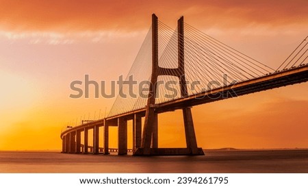 Vasco da Gamma road bridge in Portuguese capital Lisbon at sunrise. The sky is colored orange. Royalty-Free Stock Photo #2394261795