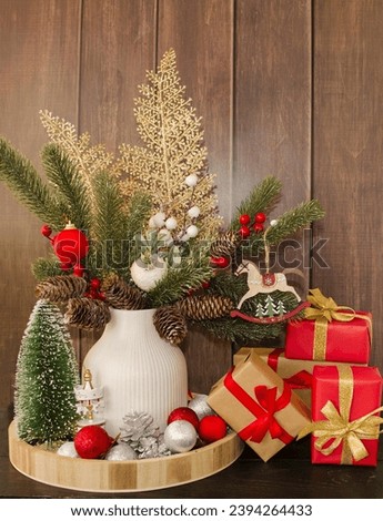 Holiday card Merry Christmas and Happy New Year.  On a wooden background there is a vase with decorated fir branches and boxes with gifts.  Home decoration concept.