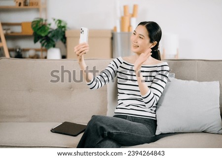 Happy Young asian woman using smartphone and tablet while seated on couch at home
