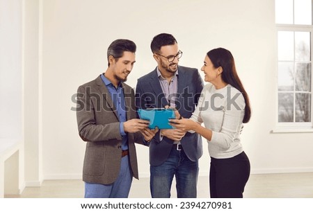 Meeting of two business partners with real estate manager in a new rented premises to sign agreement. Young smiling woman realtor gives the contract and pen to sign the transaction document.