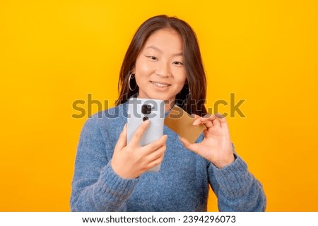 Studio photo with yellow background of a chinese woman using mobile and card to shopping online