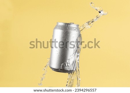 Aluminium beer or soda drinking can with water splash on light yellow background