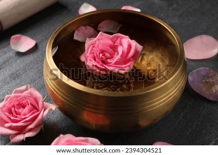 Tibetan singing bowl with water and beautiful rose flowers on gray table, closeup