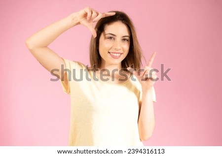 Closeup of young beautiful woman making frame with her fingers, over pink background