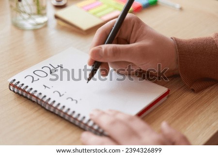 Young hands writing in notebook 2024 new year's resolutions index list over wooden table Royalty-Free Stock Photo #2394326899