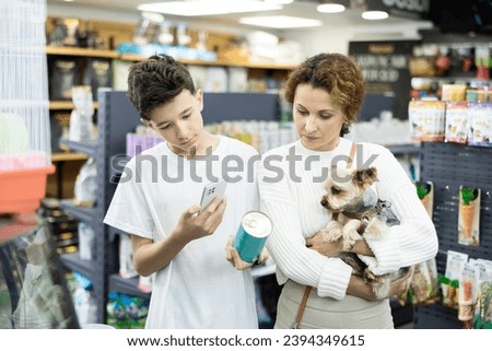 Family with Yorkshire terrier puppy is choosing soft food in tin can for small breed dog, son is photographing by phone packaging label. Teenage boy scans QR code on feed jar