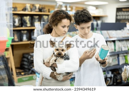 Family with Yorkshire terrier puppy is choosing soft food in tin can for small breed dog, son is photographing by phone packaging label. Teenage boy scans QR code on feed jar