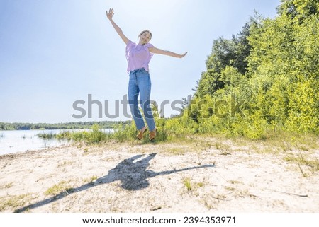 The image captures an exuberant moment as a person joyfully leaps into the air. The individual's shadow is sharply cast on the ground, suggesting the bright and clear conditions of a sunny day. They Royalty-Free Stock Photo #2394353971