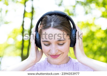 The image captures a serene moment as a young woman, adorned with headphones, enjoys her favorite melodies. Eyes closed, she appears to be lost in the harmonious embrace of music, with a gentle smile Royalty-Free Stock Photo #2394353977
