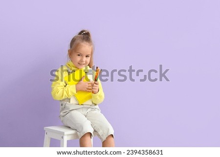 Cute little girl with notebooks, pencils and brushes on lilac background
