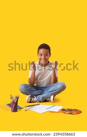 Little African-American boy with pencils on yellow background