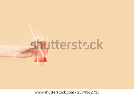 Female hand holding cup of water with red paint and artist's brush on beige background