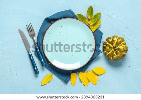 Stylish autumn table setting with leaves and pumpkin on blue background
