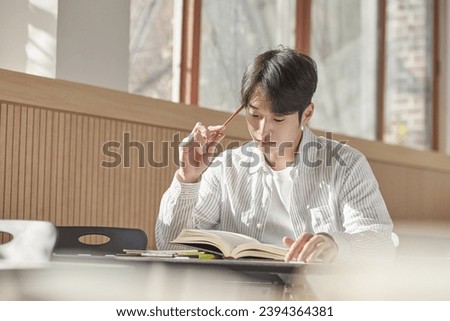 A young college student is sitting at a desk in a university classroom in South Korea, Asia. He is either reading a book or looking out of the window	
