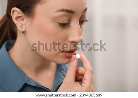 Depressed woman taking antidepressant pill on light background, closeup