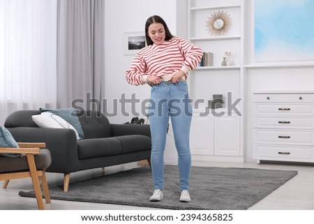 Woman trying to put on tight jeans at home Royalty-Free Stock Photo #2394365825