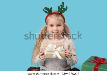Cute little girl with deer horns and gifts on blue background