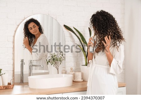 Beautiful African-American woman with hair spray near mirror in bathroom Royalty-Free Stock Photo #2394370307