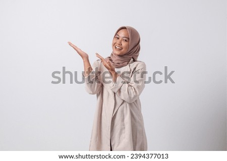 Portrait of excited Asian hijab woman in casual suit pointing and showing product in her side with finger. Businesswoman concept. Isolated image on white background