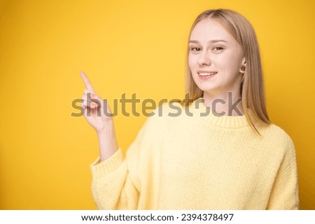 Cute girl standing on yellow background wearing sweater and pointing to place for text. Banner or advertising layout.