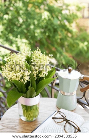 Composition with spring flowers lily of the valley, book and glasseson it and coffee pot on table. Good morning concept. Side view.