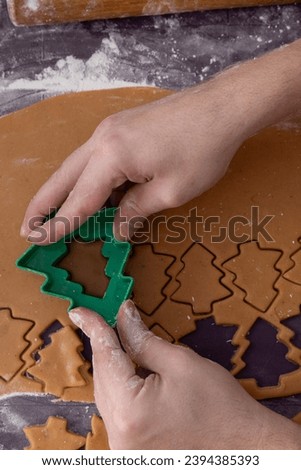 cook christmas ginger cookies. Bake gingerbread cookies shaped like Christmas trees. Human hands use a tree-shaped mold to press out cookie shapes in the dough.