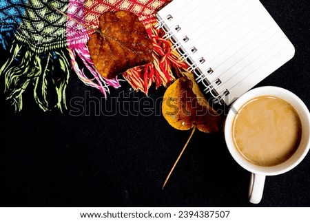 The comfort of being at home in autumn. The photo above is of a cup of hot coffee, a patchwork blanket, maple leaves, on a black isolated background with copy space