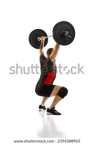 Side view. Muscular, athletic man, weightlifter training, lifting heavy barbell against white background. Concept of sport, strength, gym, healthy lifestyle, power and endurance, weightlifting
