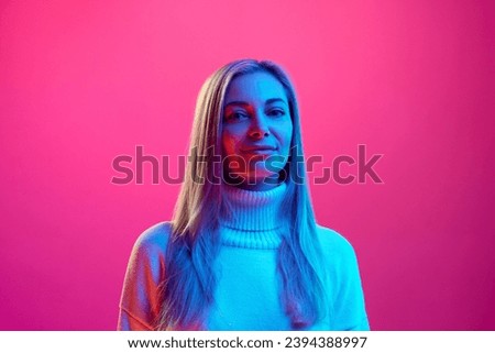 Close up portrait of young attractive calm woman in knitted warm sweater against pink background in neon light. Concept of beauty, human emotions, facial expression, fashion and style.