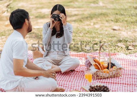 Happy asian couple travel. Woman taking photo of his boyfriend picnic time in park holidays vacation