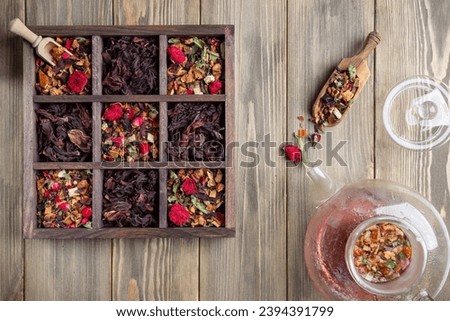 Dry herbal tea with fruits and flowers in wooden box on wooden background. Top view.