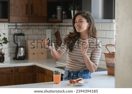 Young woman influencer vlogging over her smartphone in her modern home kitchen