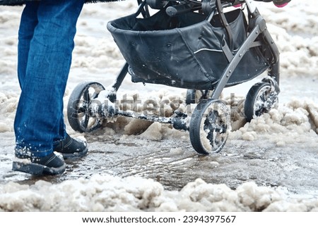 Woman push baby stroller through wet snow in winter season. Woman with baby carriage walk through snowy icy road after heavy snowfall in the city. Wheels of the baby stroller stuck on sleet Royalty-Free Stock Photo #2394397567