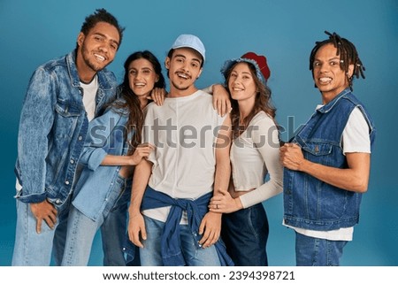 diverse group of excited interracial friends in trendy and denim clothes looking at camera on blue