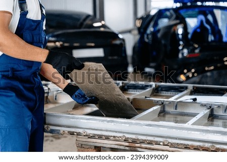 Male mechanic engineer working with car battery module in workshop. Empty pack of battery cells module on platform removed from car for repair. Royalty-Free Stock Photo #2394399009
