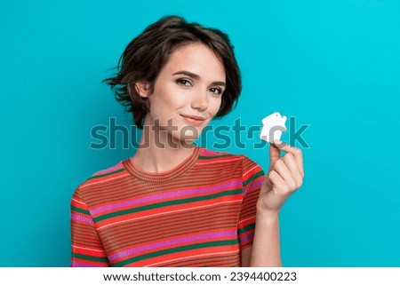 Portrait of cheerful girl with bob hairstyle wear stylish t-shirt fingers showing small white house isolated on turquoise color background