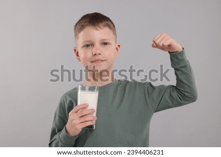 Cute boy with glass of fresh milk showing his strength on light grey background