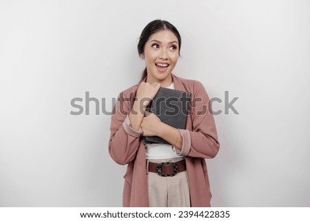A thoughtful young Asian woman pupil wearing cardigan while holding books and looking aside to copy space, isolated by white background. 