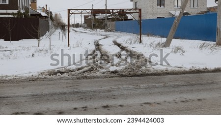 Snowy road in countryside. Drifts on an unplowed snow-covered country road through cottage community. Car traces in winter. Concept of dangerous driving in winter, ice, snowfall and snow storm