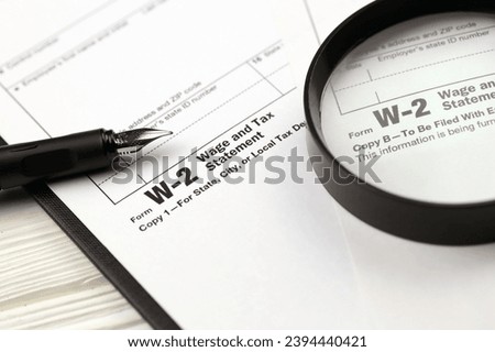 IRS Form W-2 Wage and Tax Statement blank on A4 tablet lies on office table with pen and magnifying glass close up Royalty-Free Stock Photo #2394440421