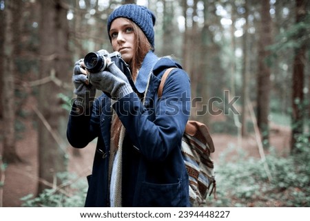 Young beautiful woman in warm clothing and backpack, taking photos in forest during autumn, winter. Lifestyle concept.