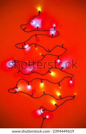 Christmas tree, made with dark string of lights, twinkling, drawn on a flat surface. Red background, colorful lamps..
 Royalty-Free Stock Photo #2394449619