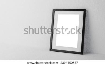 Black rectangular picture frame on white wall with blank paper mockup of diploma, certificate, photo or painting on neutral background