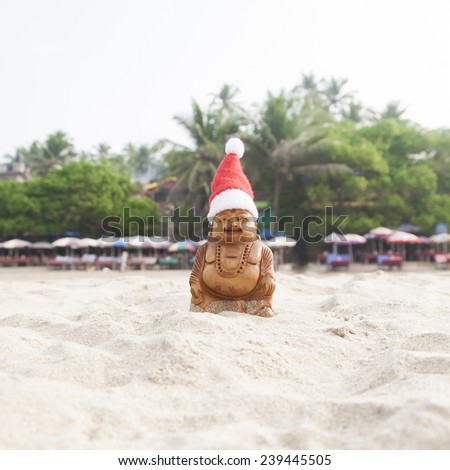 Budda statuette in the christmas bonnet on the beach. Tropical jungle in the background.