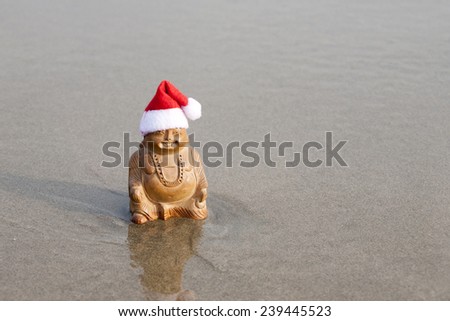 Budda statuette in the christmas bonnet on the beach. Waves in the background.