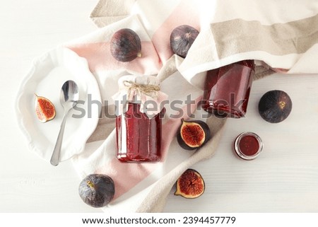 Figs, jars of jam and towel on light background, top view