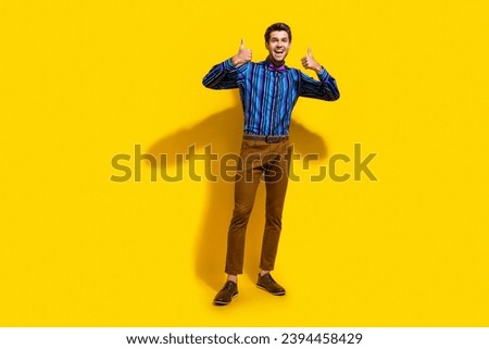 Full size photo of satisfied optimistic guy dressed striped shirt brown trousers showing thumbs up isolated on yellow color background