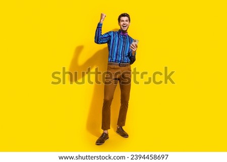 Full size photo of overjoyed guy dressed striped shirt raising fist up win gambling hold smartphone isolated on yellow color background