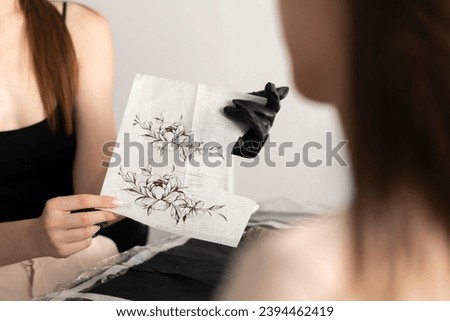 female tottooist showing sketch of a tattoo to her client in the office 